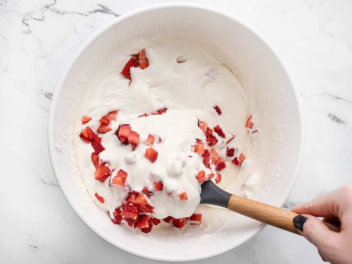Folding chopped strawberries into whipped cream mixture.