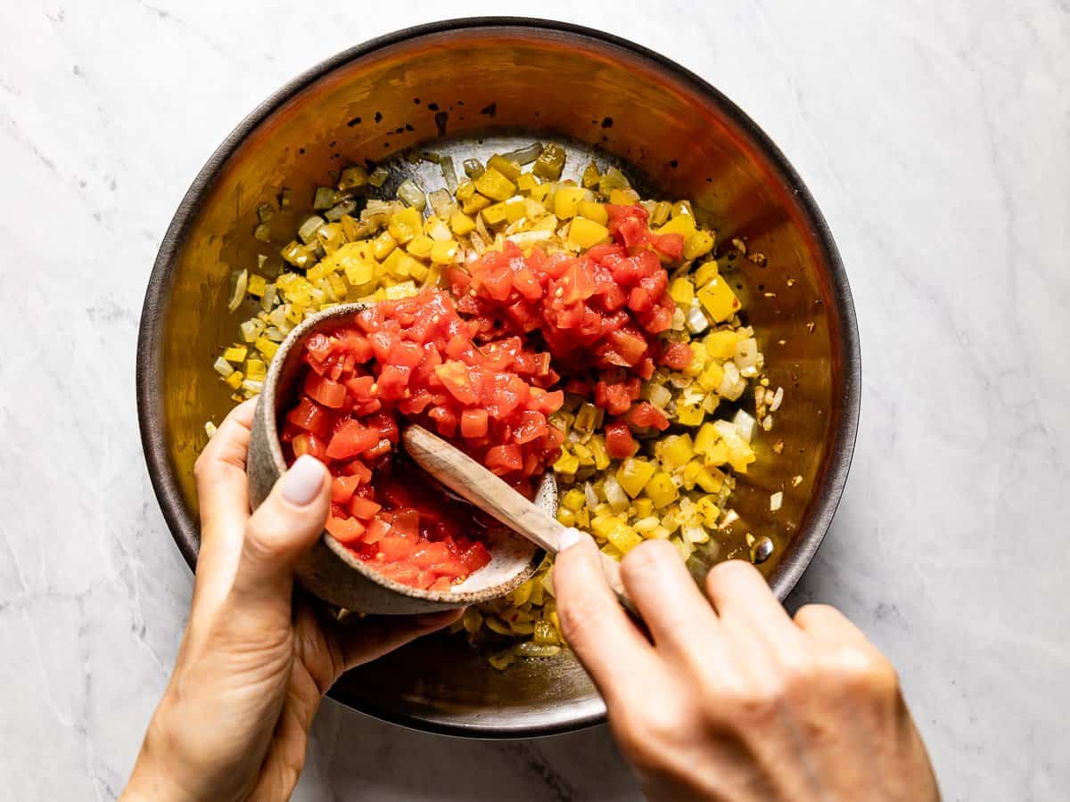 Diced tomatoes being added to the skillet from a bowl.