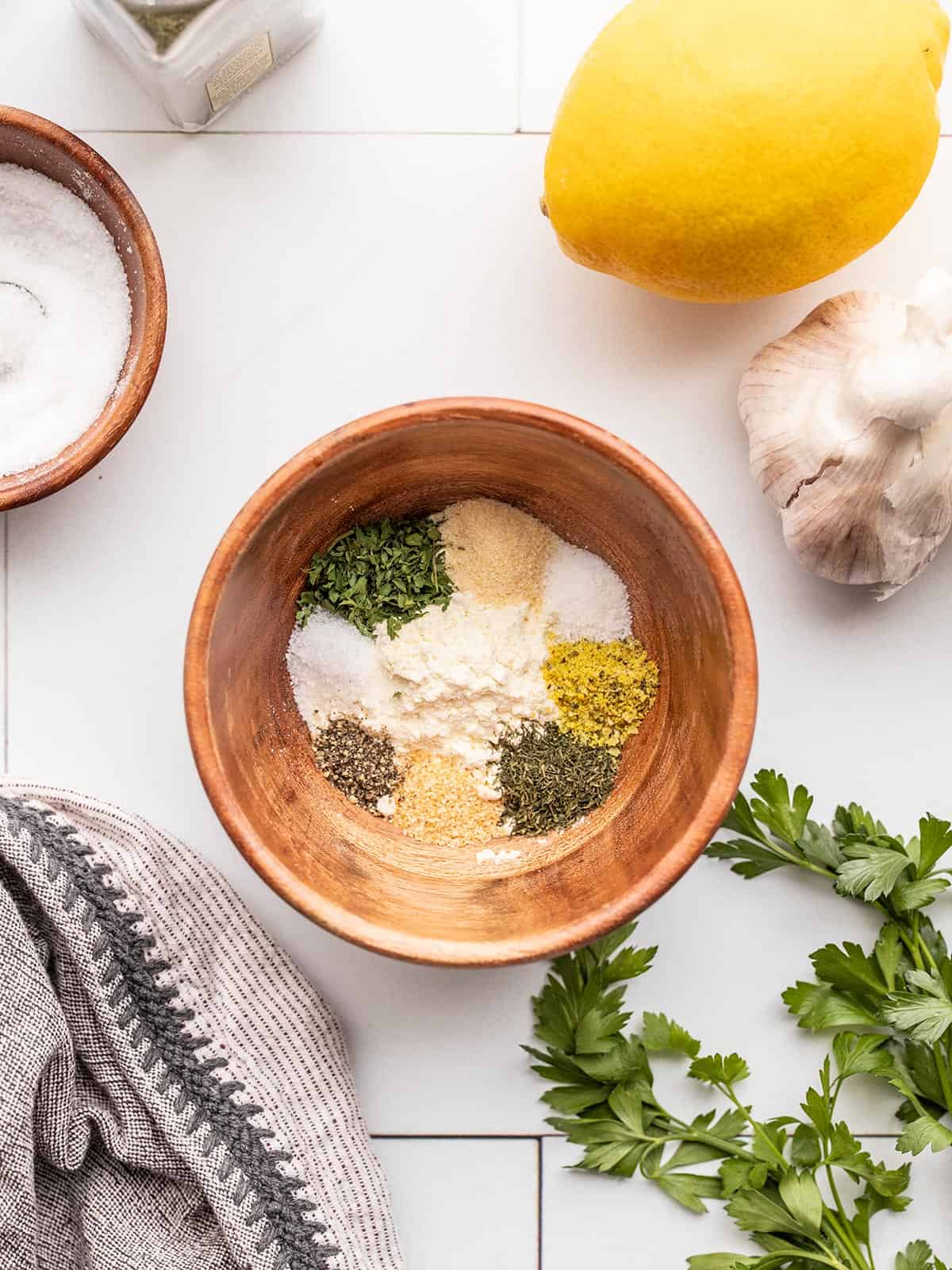 Ranch seasoning mix ingredients in a small wooden bowl with lemon, garlic, and parsley on the sides