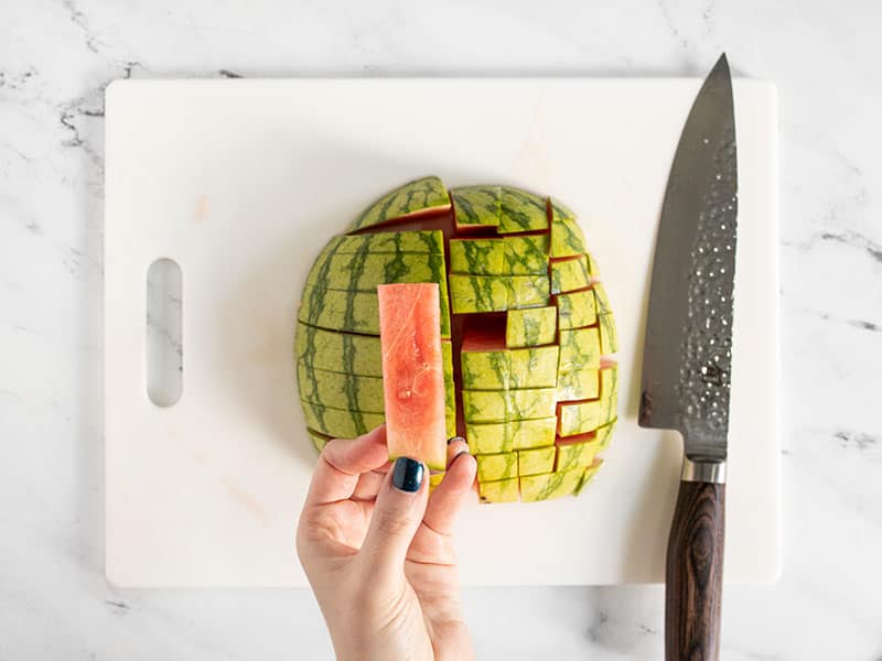 Watermelon cut into batons, a hand holding one close to the camera