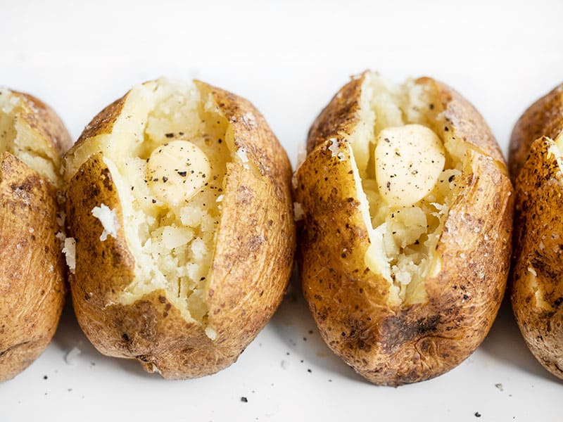 Side view of baked potatoes lined up, seasoned with pepper and butter
