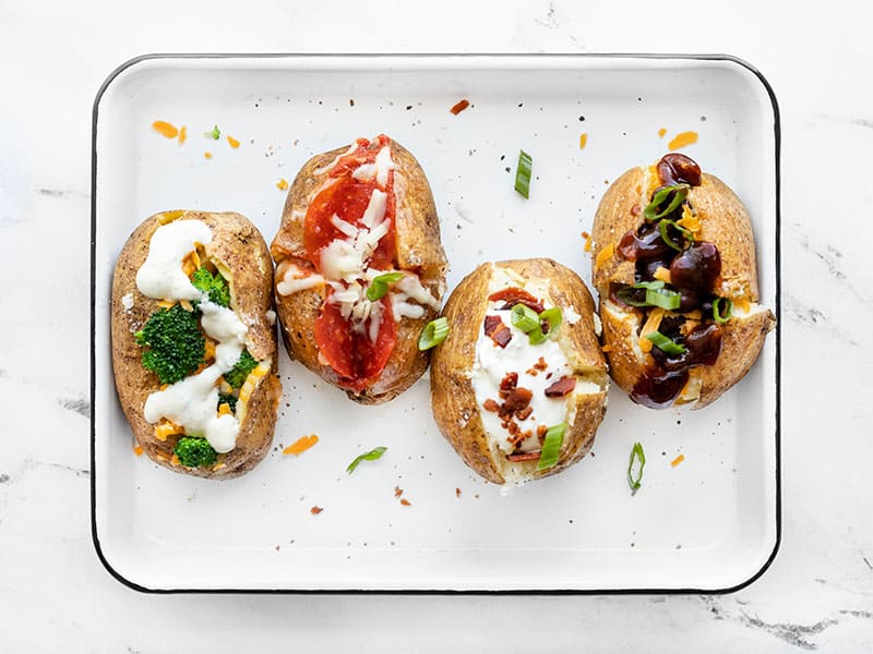 Four baked potatoes on a baking sheet, each with different toppings