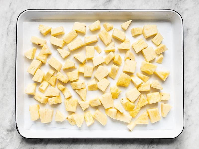 Fresh pineapple chunks spread out on a parchment lined baking sheet.