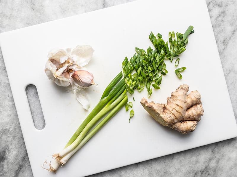 Garlic, sliced green onion, and ginger on a cutting board.