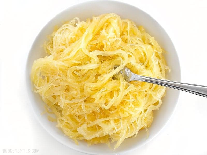 Cooked spaghetti squash strands in a white bowl with a fork