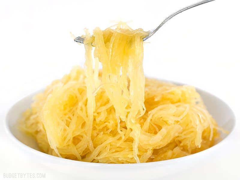 A fork lifting spaghetti squash out of a bowl, as seen from the side.