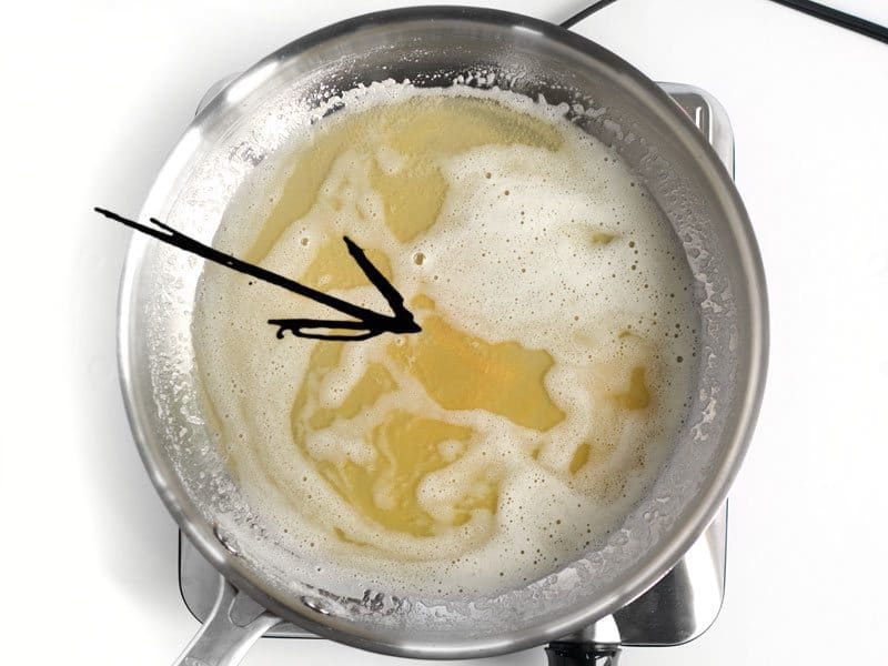 Melted butter in the skillet, an arrow pointing at butter solids beginning to turn golden brown
