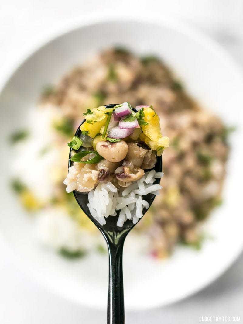 Close up of a spoonful of Coconut Jerk Peas with rice and pineapple salsa