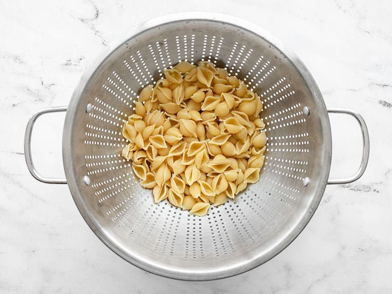 draining shell pasta in a metal colander