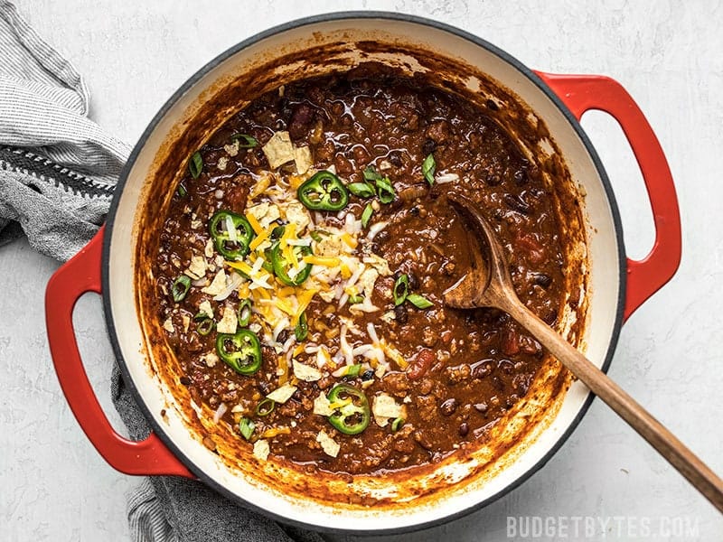 A pot of Chili with Toppings and a wooden spoon