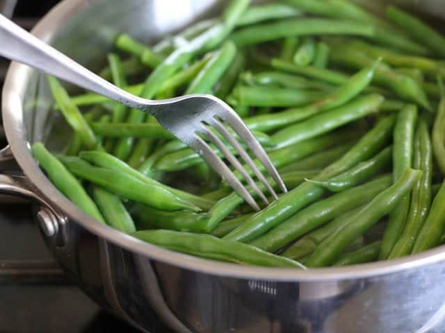 A fork testing the texture of the green beans