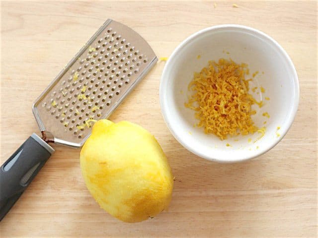 Zested lemon next to a microplane and a bowl full of zest
