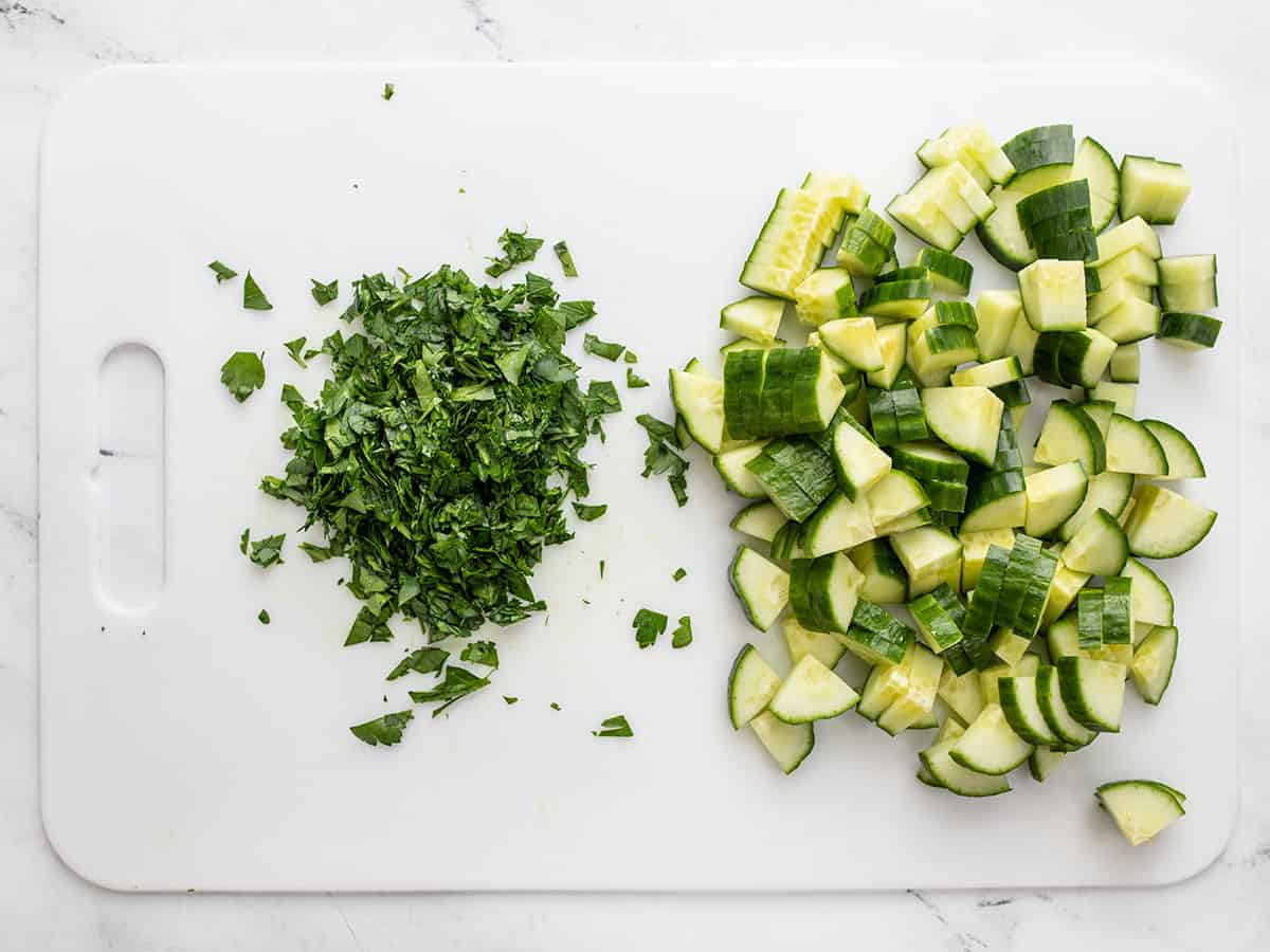 Chopped parsley and cucumber on a cutting board.
