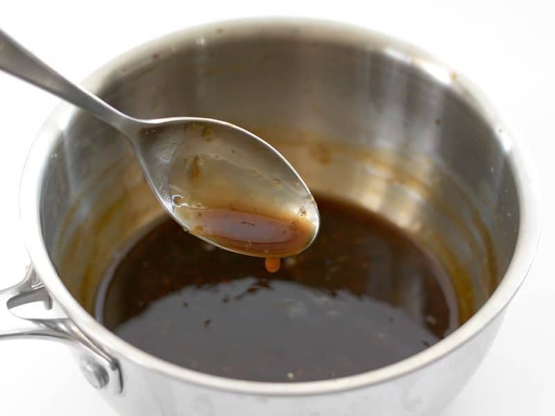 Thickened Orange Sauce dripping off a spoon into the pot