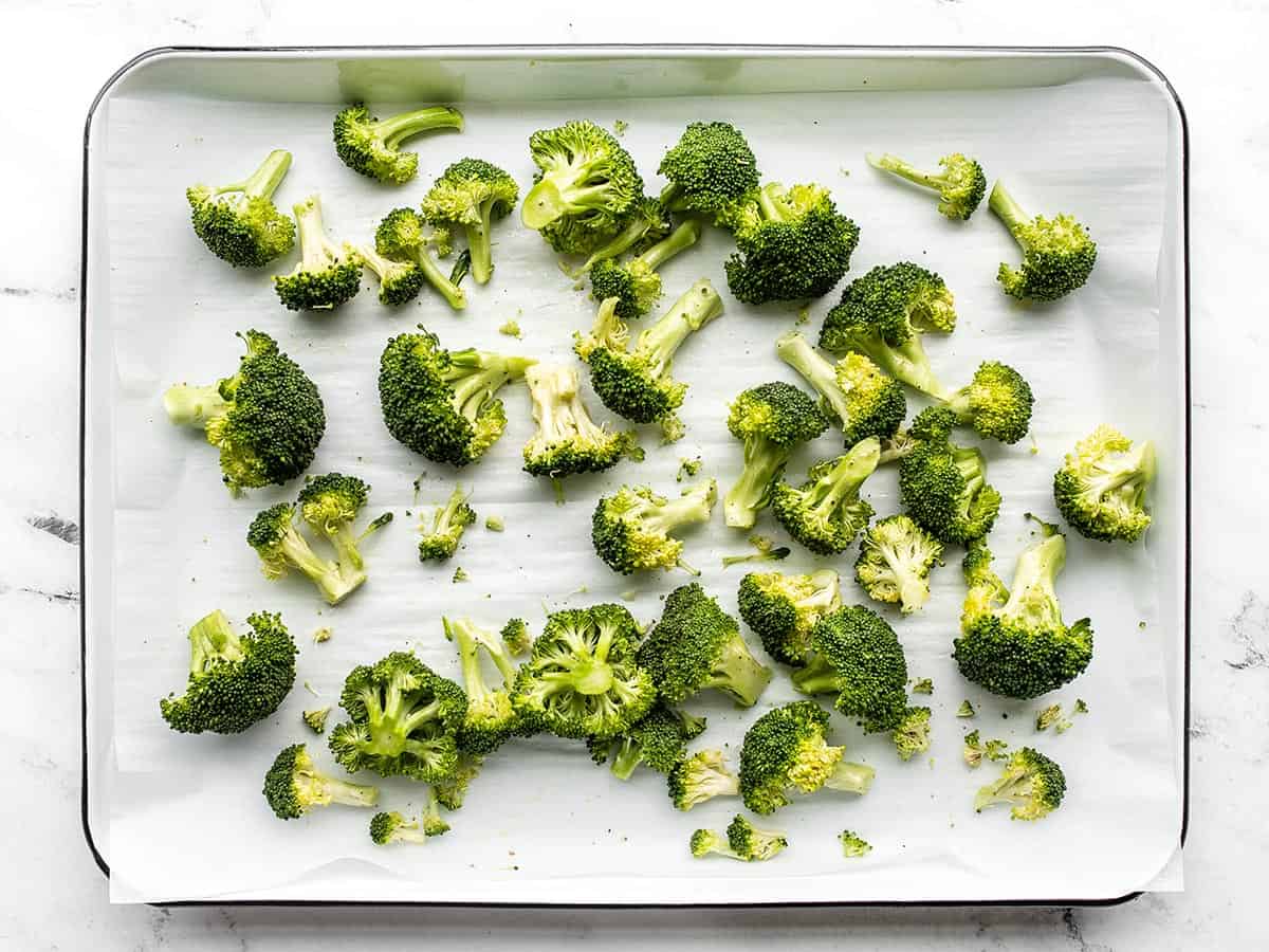 Seasoned broccoli florets on a parchment lined baking sheet