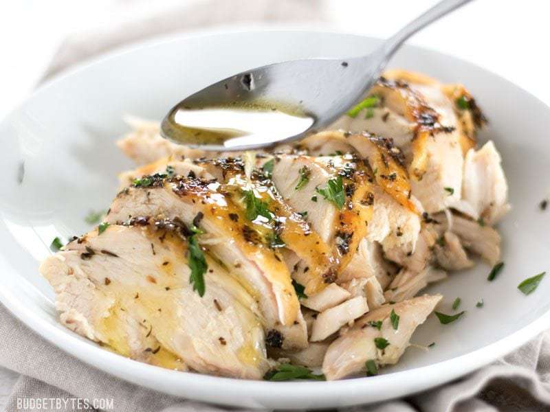 Juices being spooned over sliced Herb Roasted Chicken Breast in a bowl