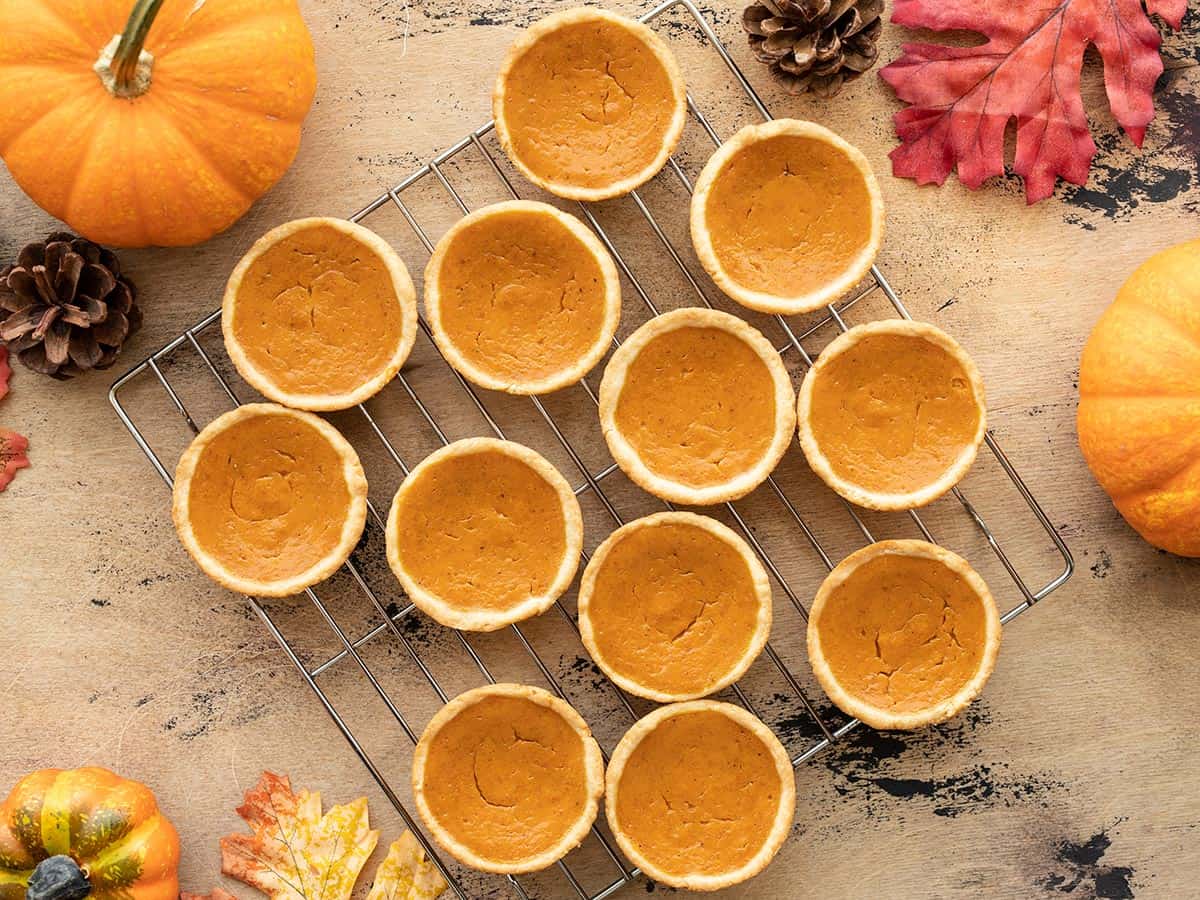 Mini Pumpkin Pies on a cooling rack next to pumpkins and leaves