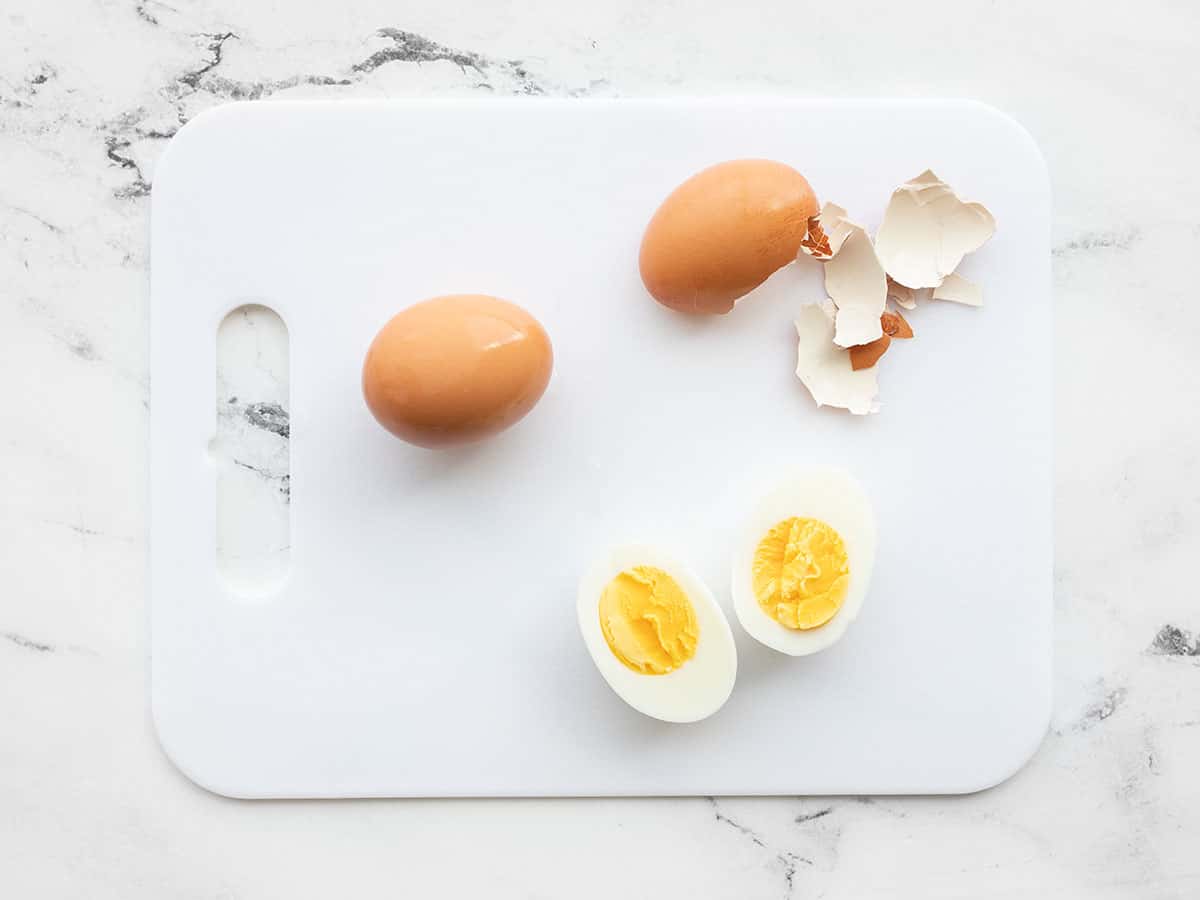 Two eggs on a cutting board, one peeled and cut in half