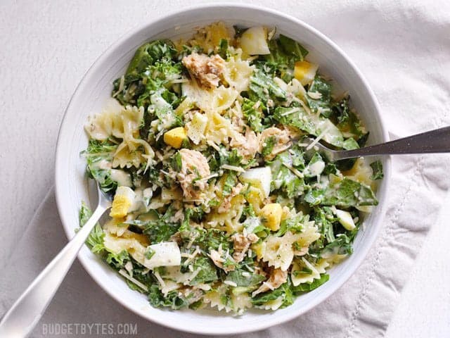 Kale and salmon caesar salad tossed and coated in dressing, in a bowl with two forks