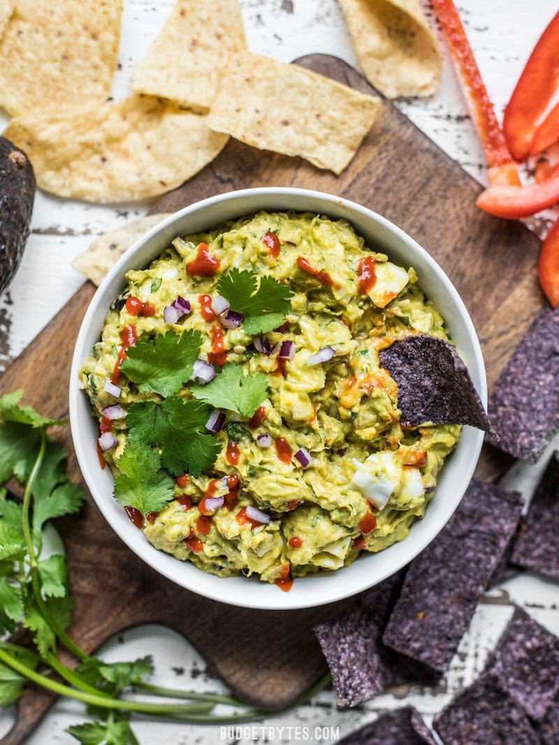 Top view of a bowl of loaded guacamole with chips on the side 