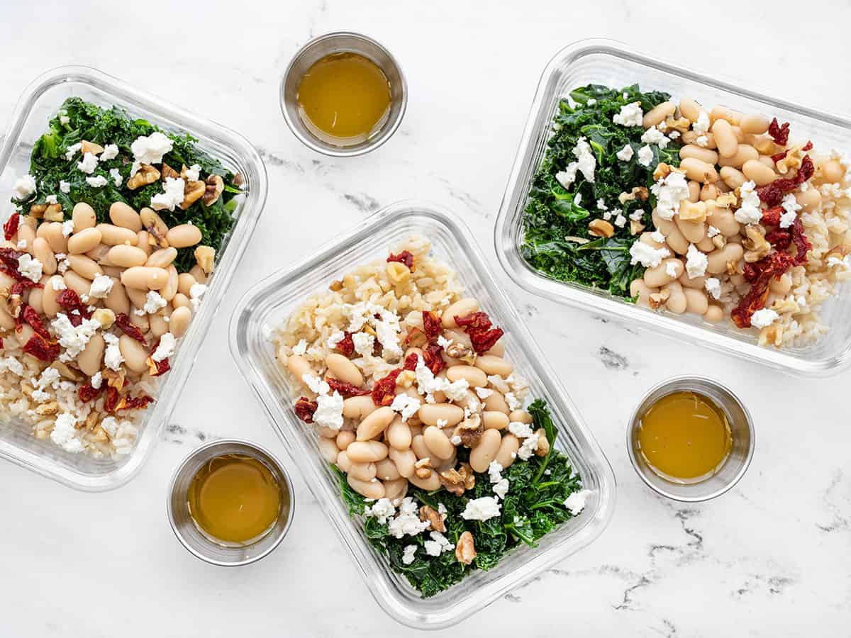 three glass meal prep containers filled with kale and white bean power bowls
