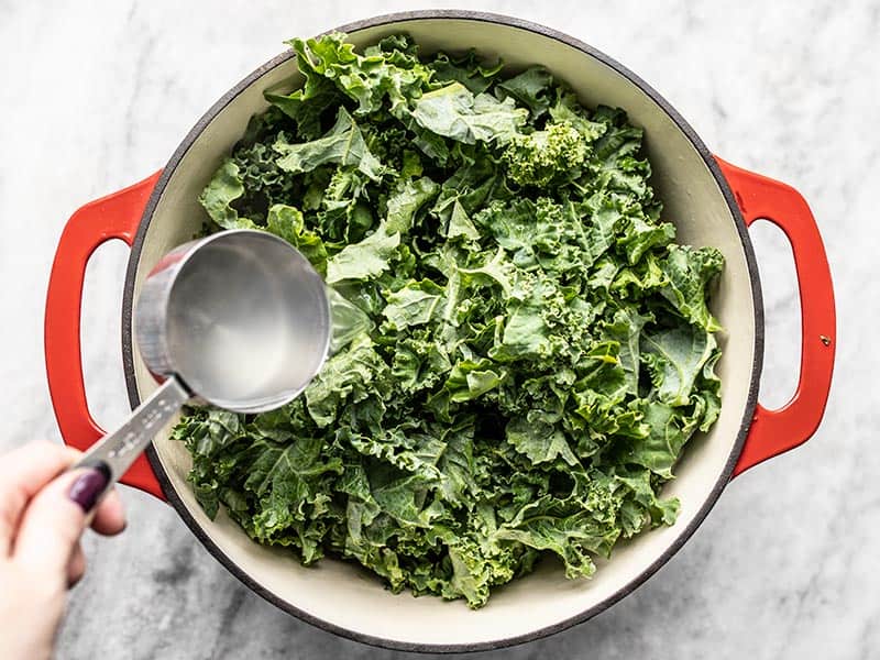Fresh kale in the pot with pasta water being poured over top.