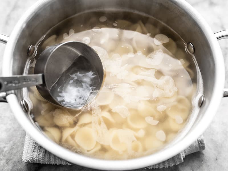 Starchy pasta water being removed from a pot of cooked orecchiette