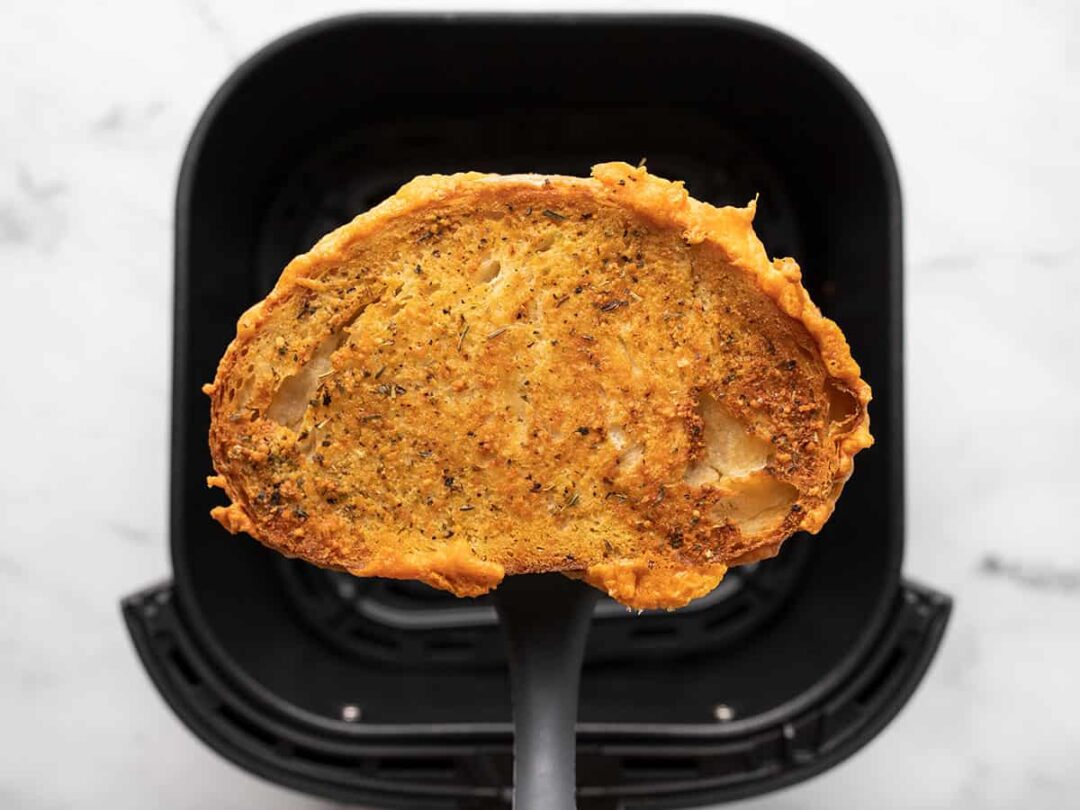 Air fryer grilled cheese on a spatula over an air fryer basket.
