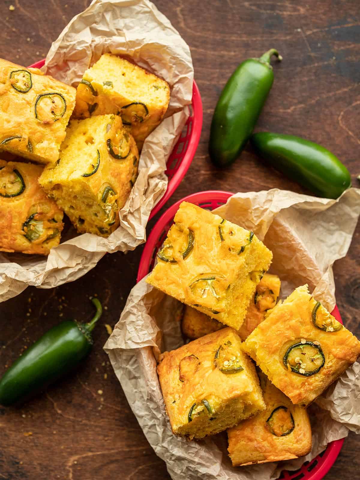 Two baskets of jalapeño cornbread pieces with whole jalapeños on the sides