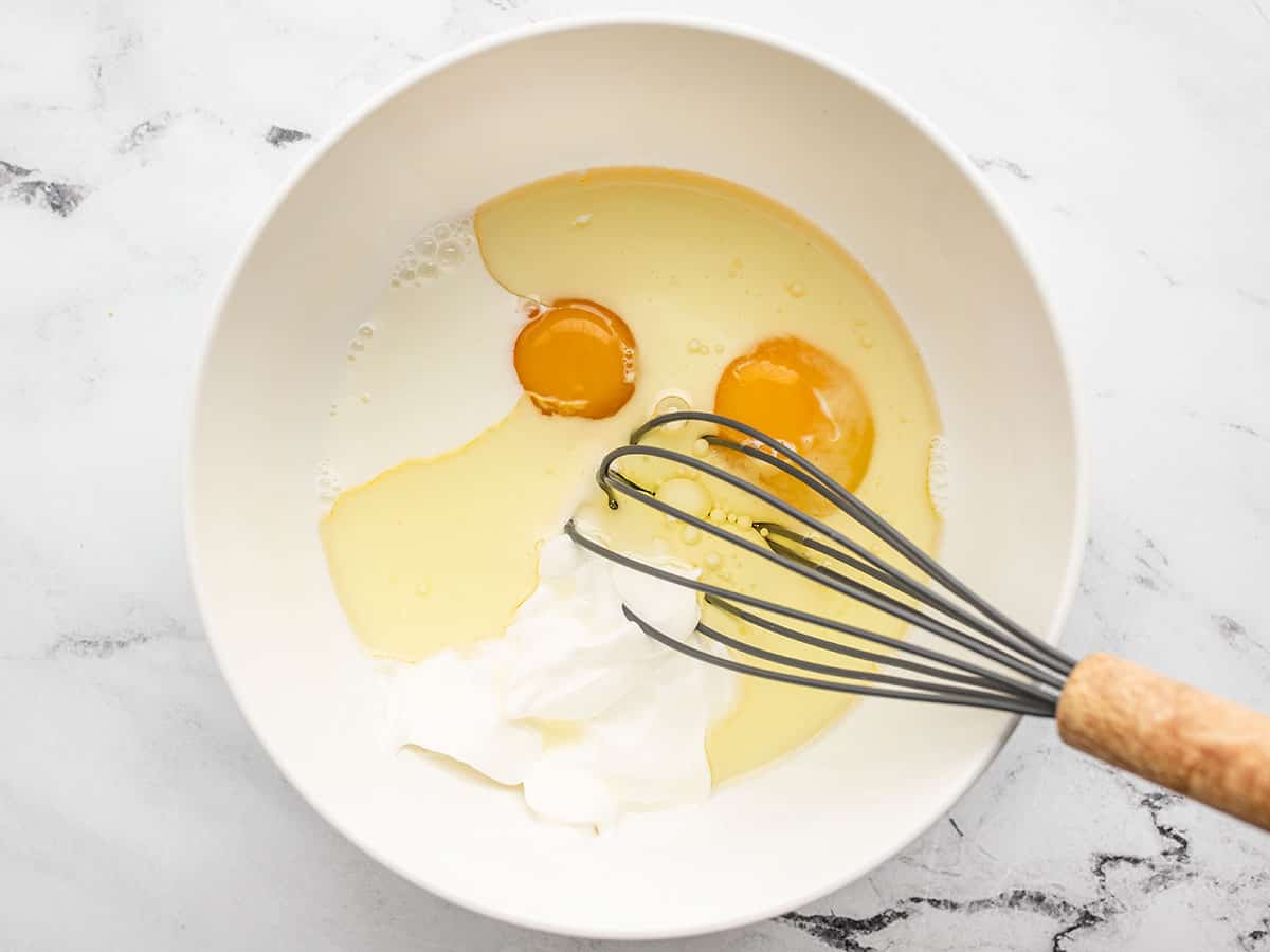 Eggs oil and milk in a bowl with a whisk