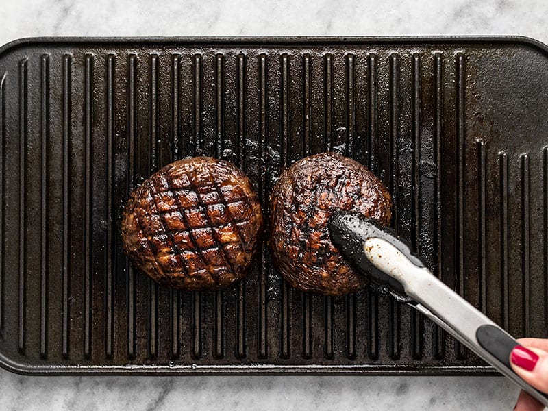 Grilled Marinated Portobello Mushroom Burgers on a grill pan with tongs.