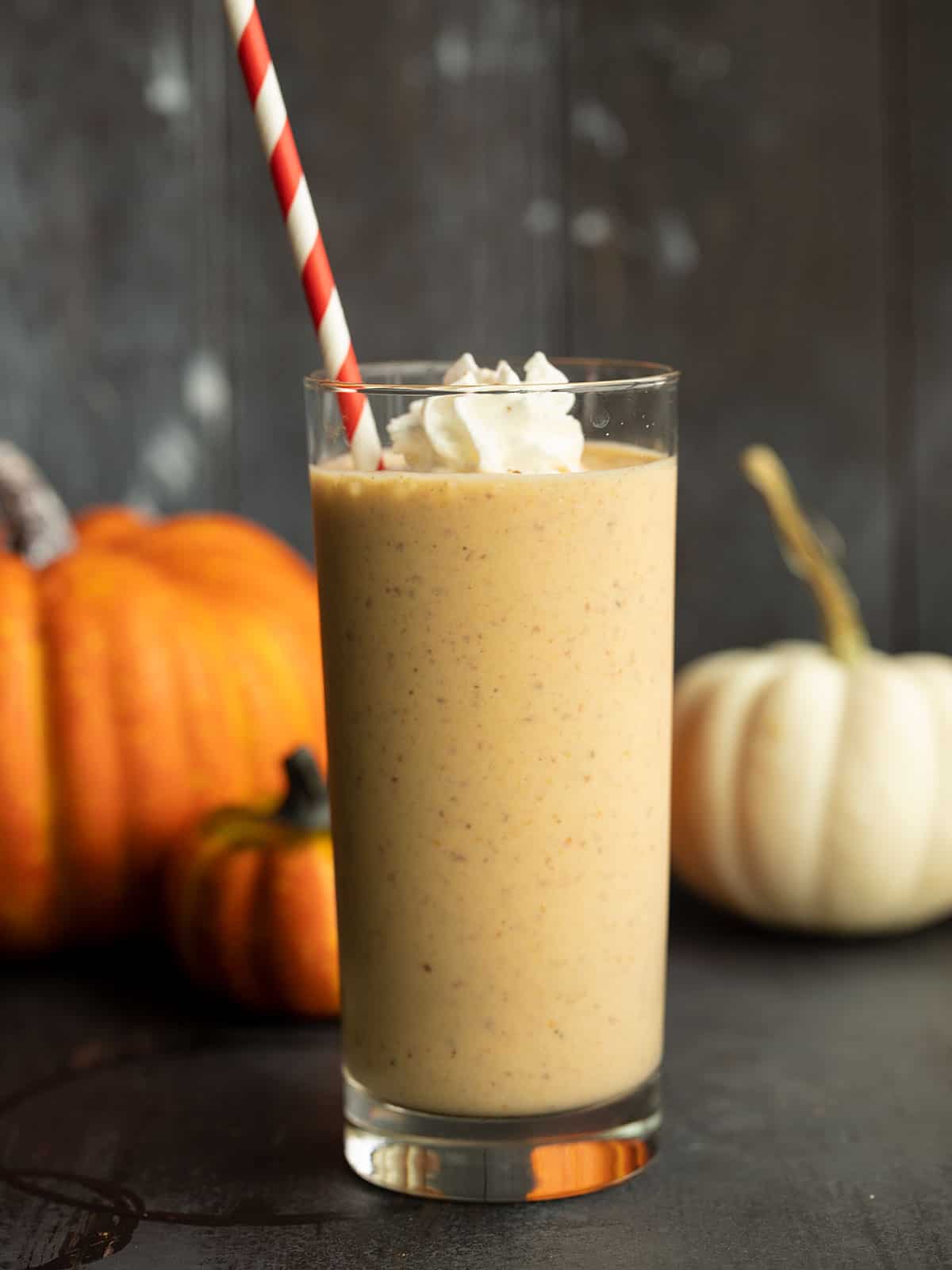 side view of a pumpkin smoothie in a tall glass with whipped cream and a straw