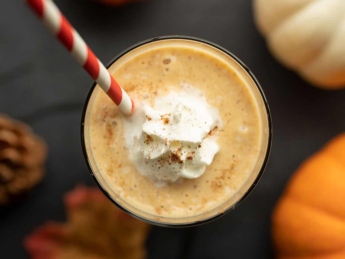 overhead view of pumpkin pie smoothie in the glass with a straw and whipped cream