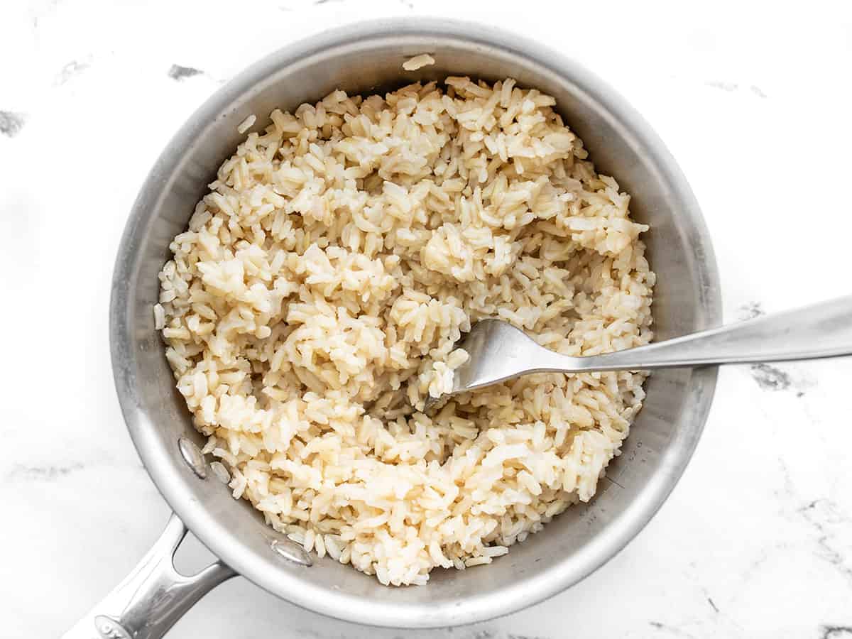 Cooked rice being fluffed with a fork in a saucepot