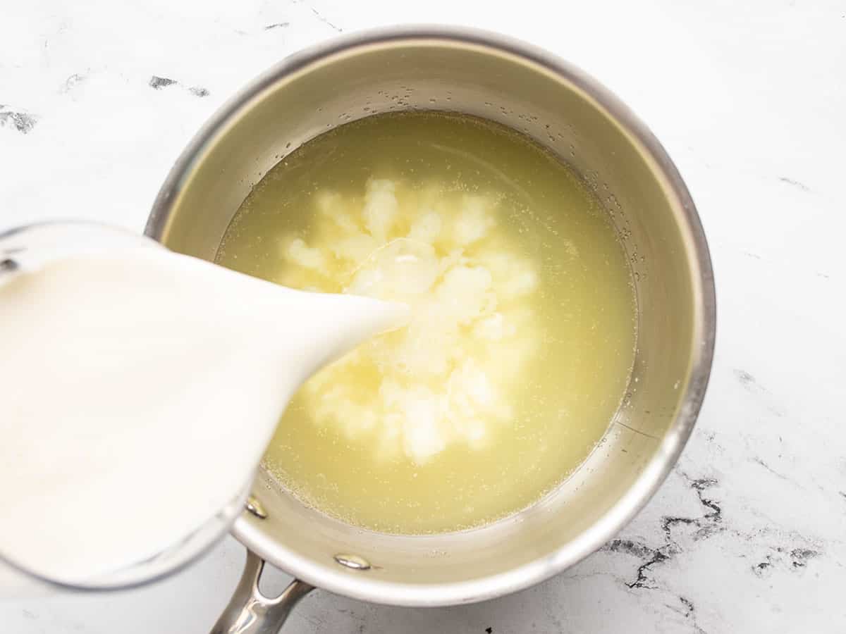 Milk being poured into a pot with chicken broth