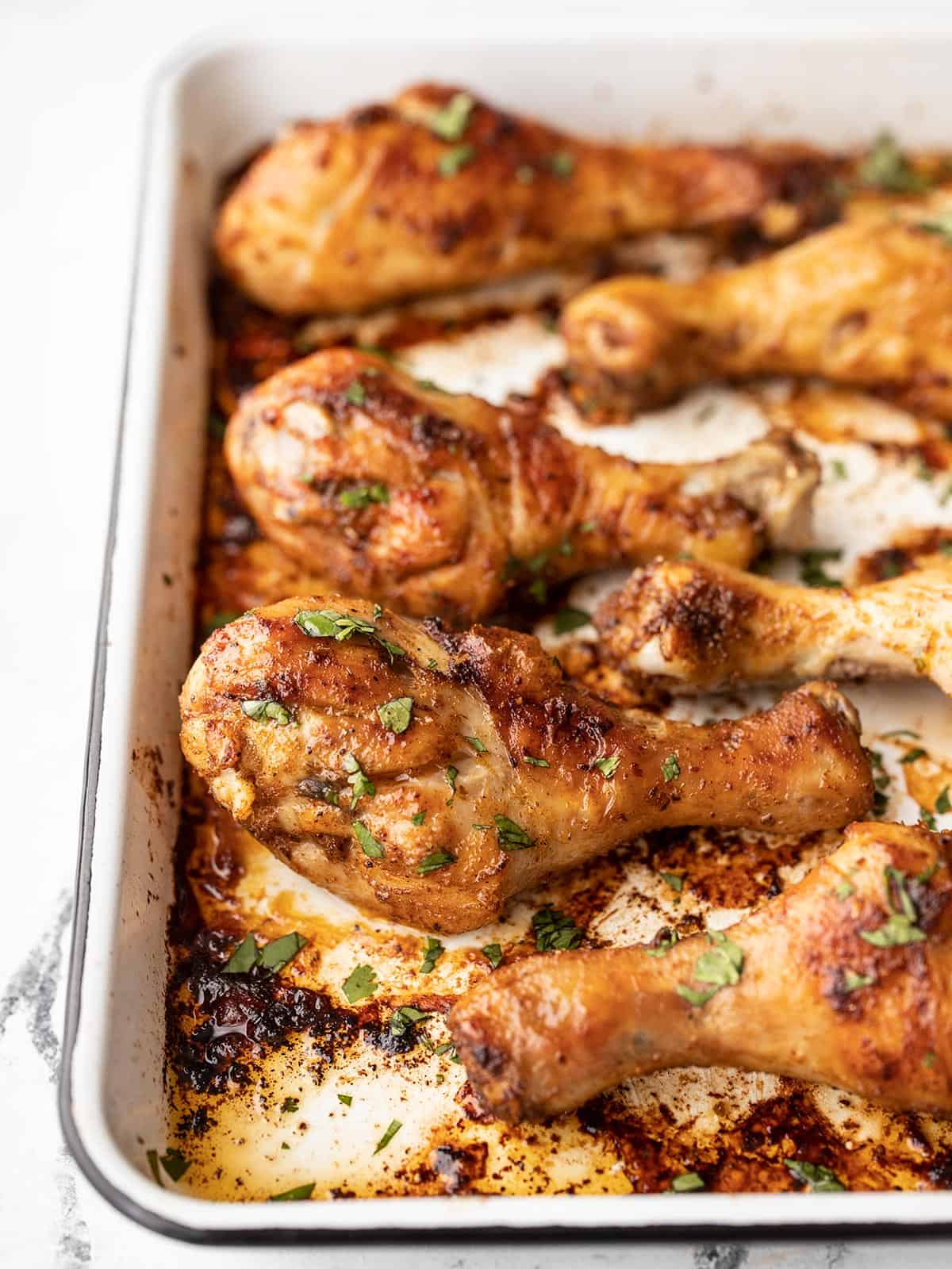 Close up side view of oven baked chicken drumsticks on a baking sheet