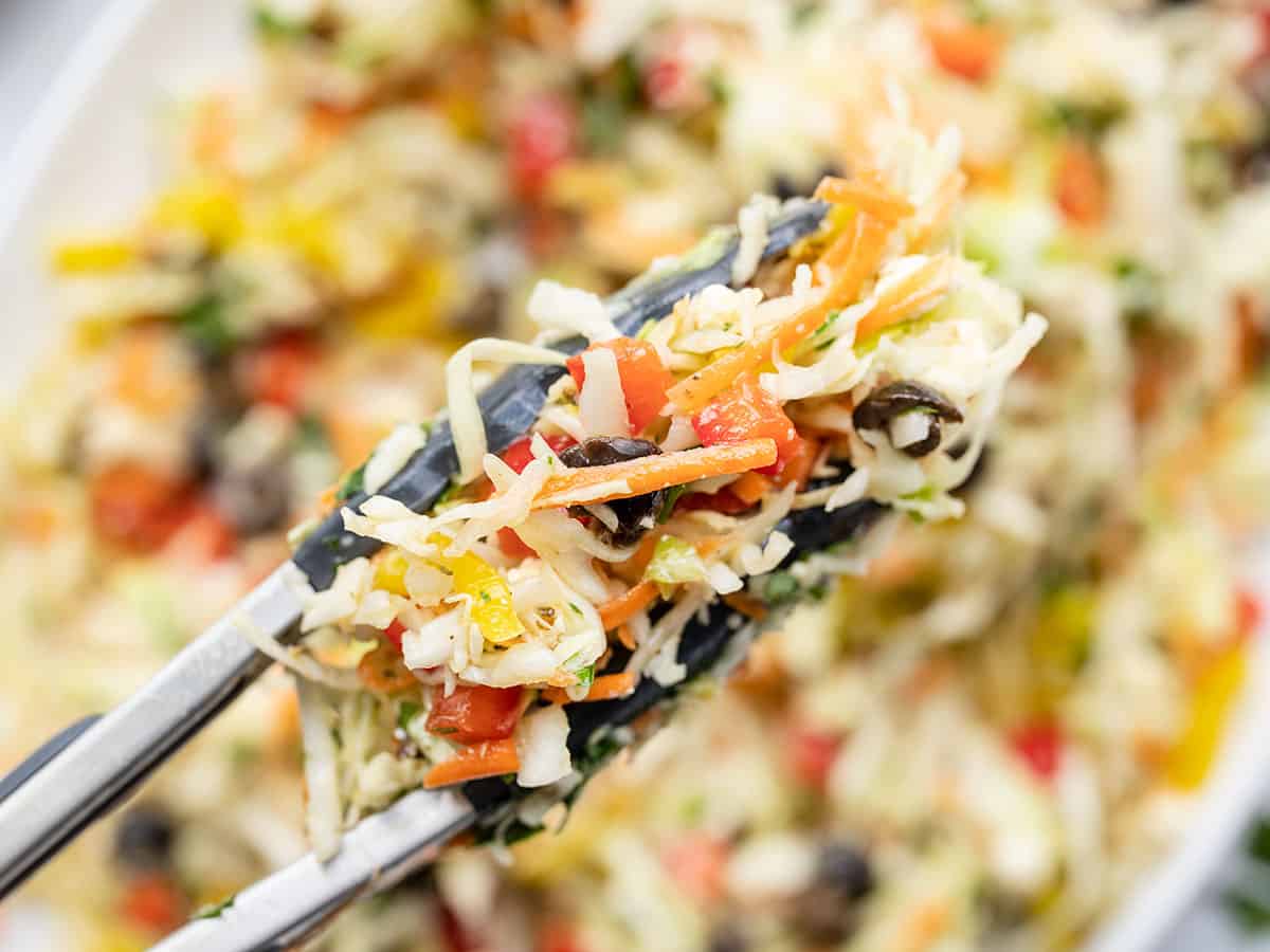 Close up of mediterranean coleslaw in tongs with the serving dish in the background