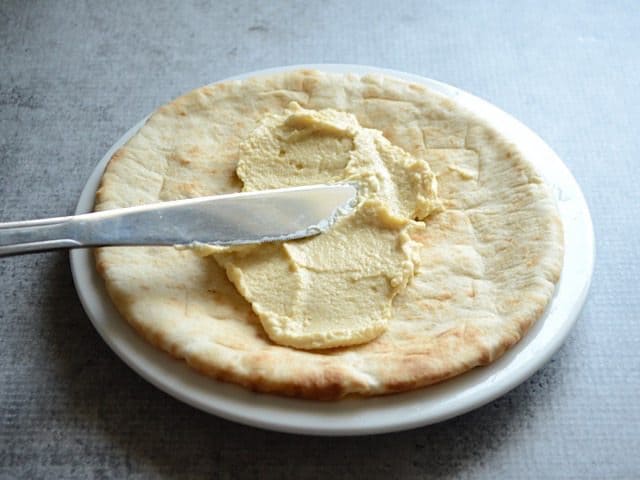 Hummus being spread onto pita