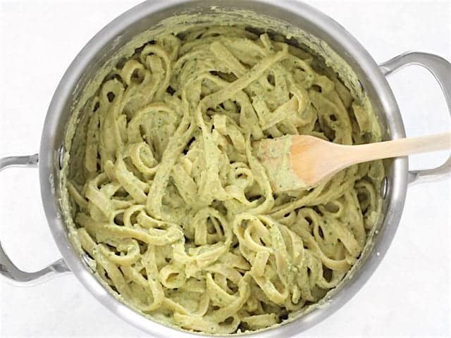 Parsley Scallion Hummus stirred into the pasta, a wooden pasta fork in the pot