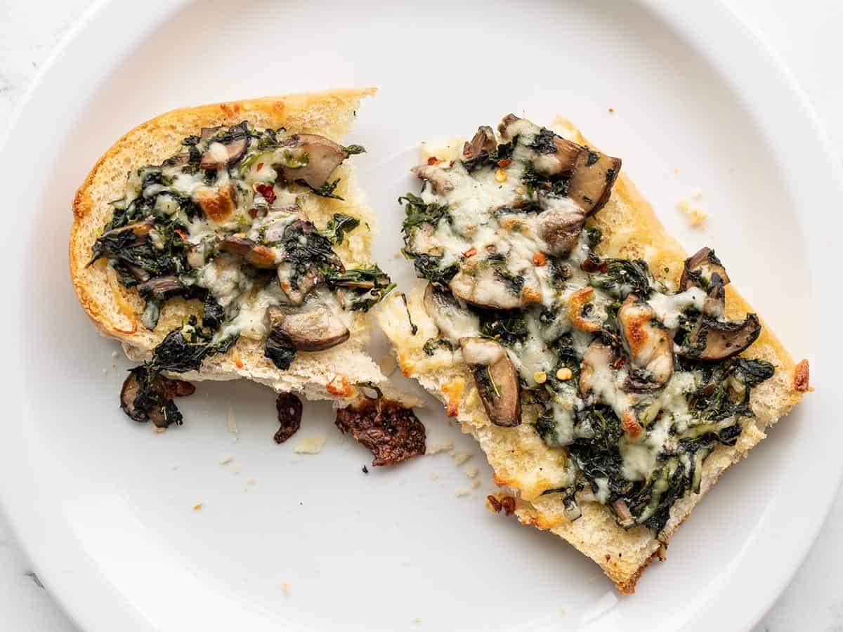 a spinach mushroom french bread pizza broken in half on a plate.