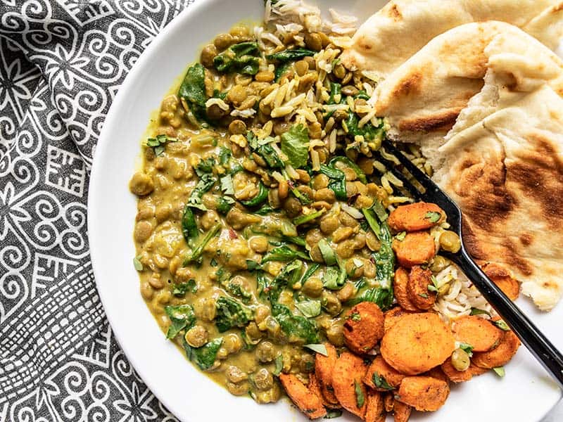 Creamy Coconut Curry Lentils with spinach on a plate with rice, naan, and curry roasted carrots.