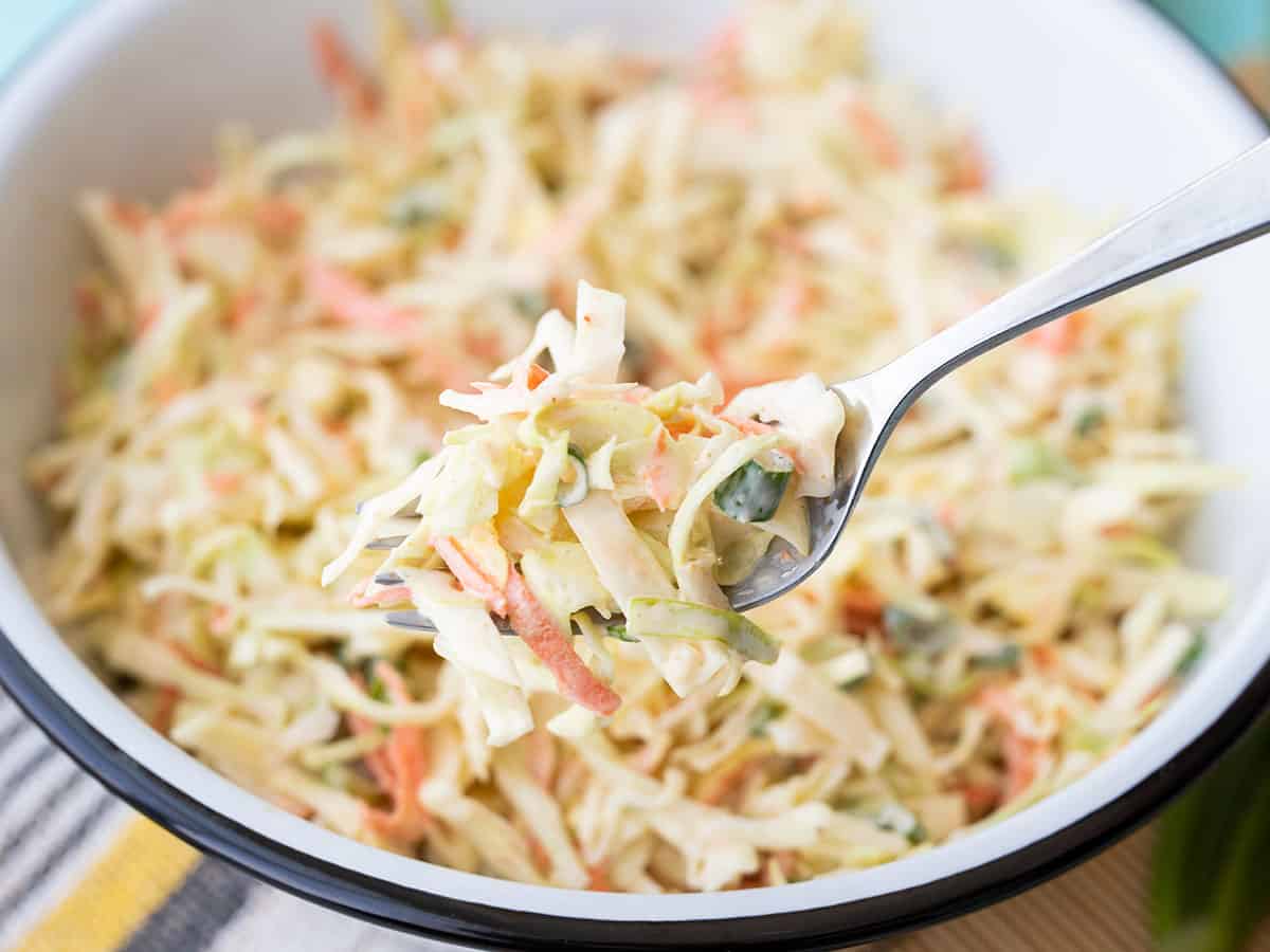 Closeup of a forkful of cumin lime coleslaw with the bowl in the background