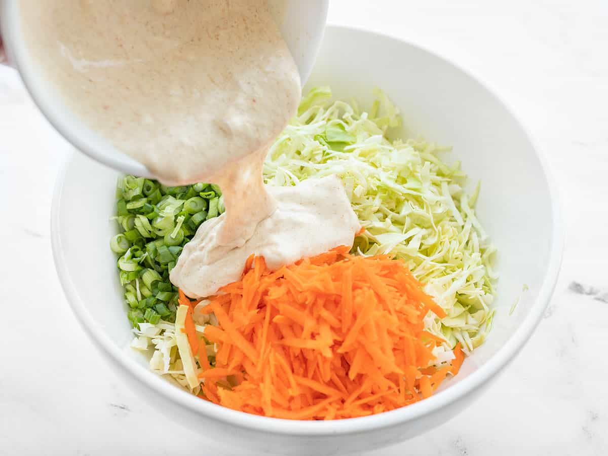 coleslaw dressing being poured over the vegetables in the bowl