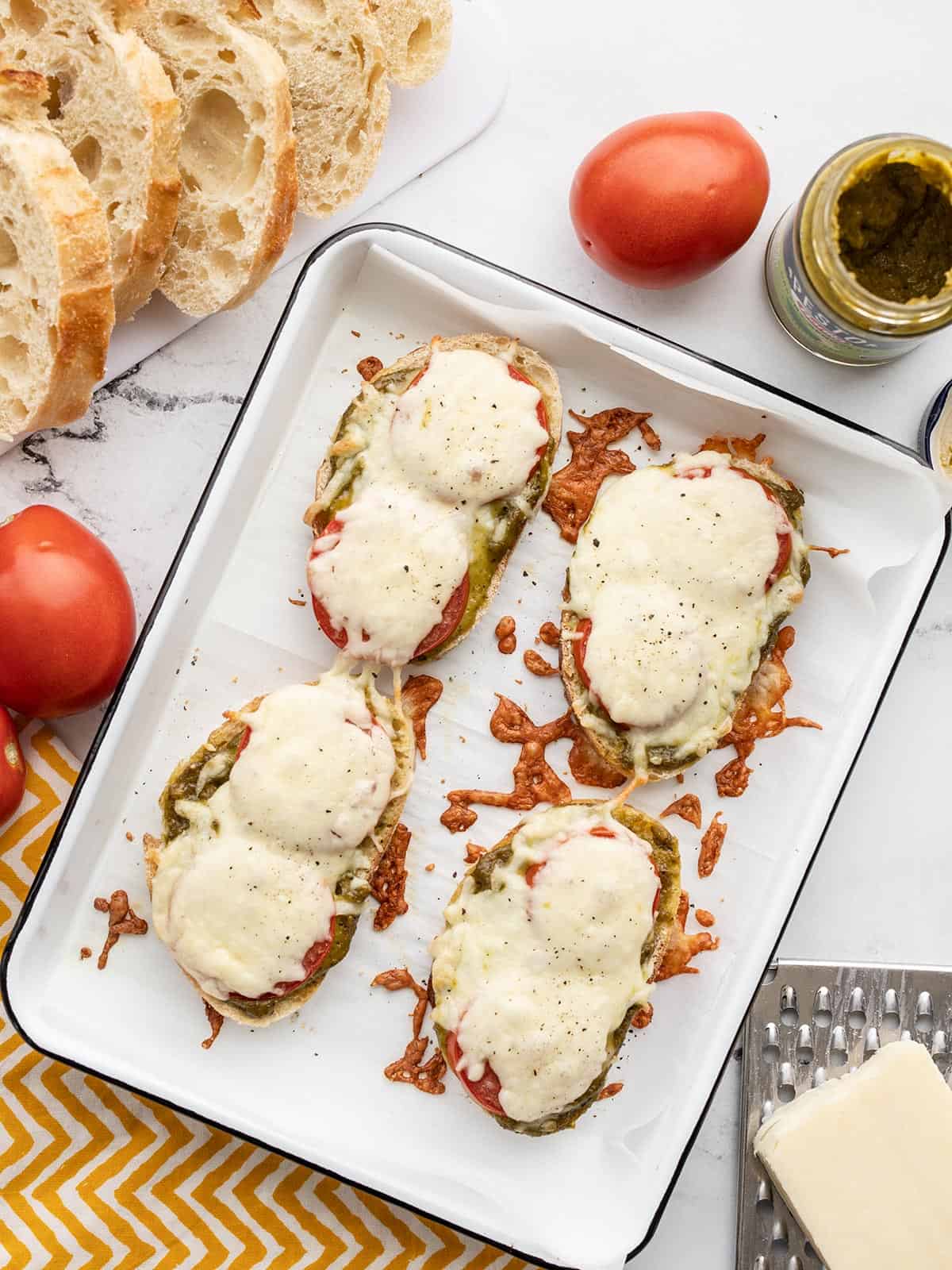 Pesto cheese toast on a baking sheet with bread, tomatoes and cheese on the sides