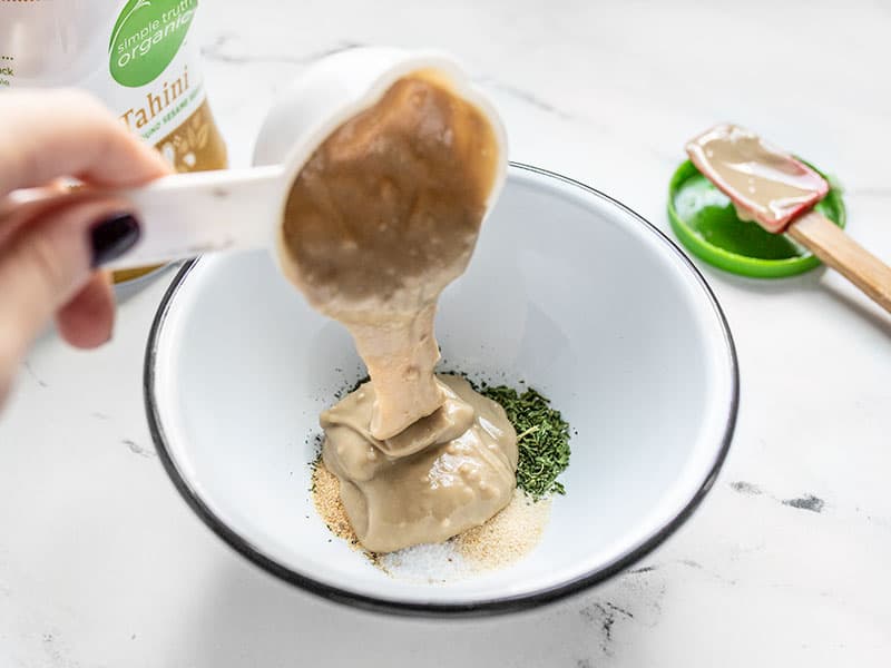 Tahini being poured into bowl with the herbs.