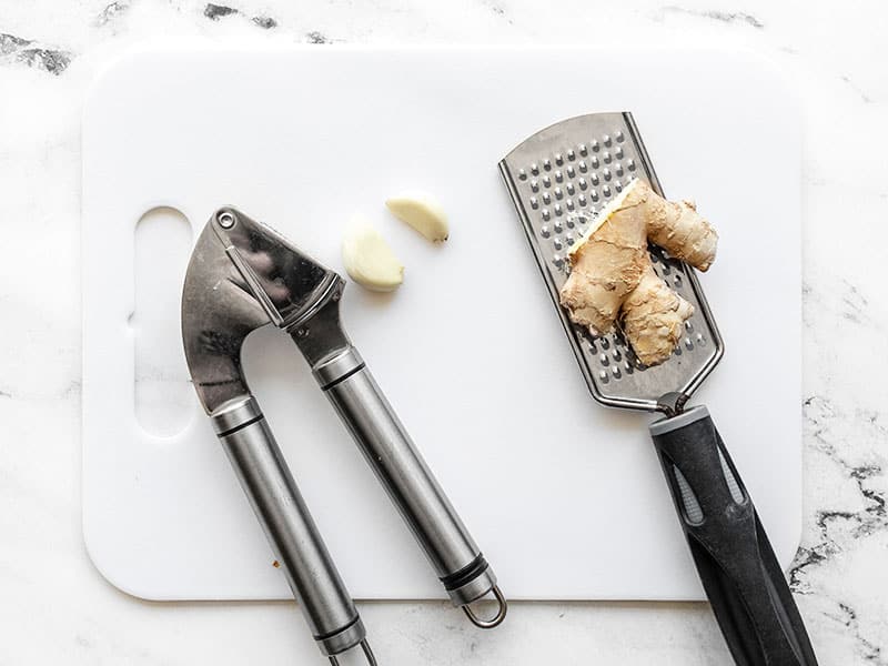 garlic press with two cloves of garlic, and fresh ginger with a microplane