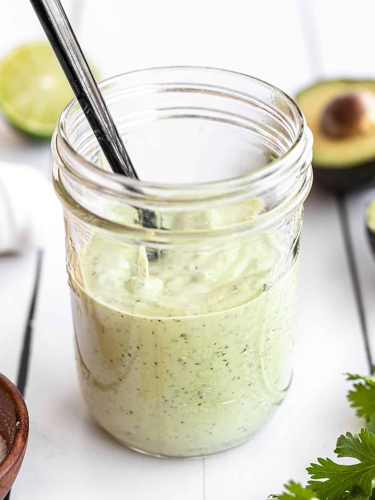 Creamy avocado dressing in a mason jar with a black spoon in the center