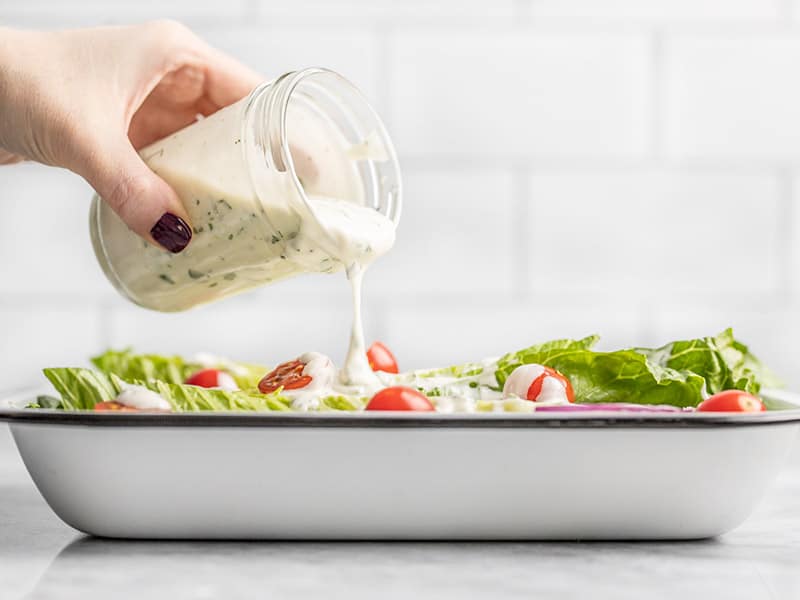 Homemade Ranch Dressing Being Poured onto a salad from a jar, viewed from the side.