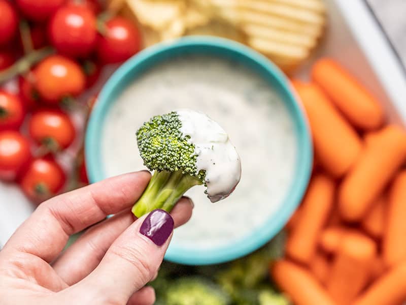Close up of a broccoli floret dipped in homemade ranch dressing