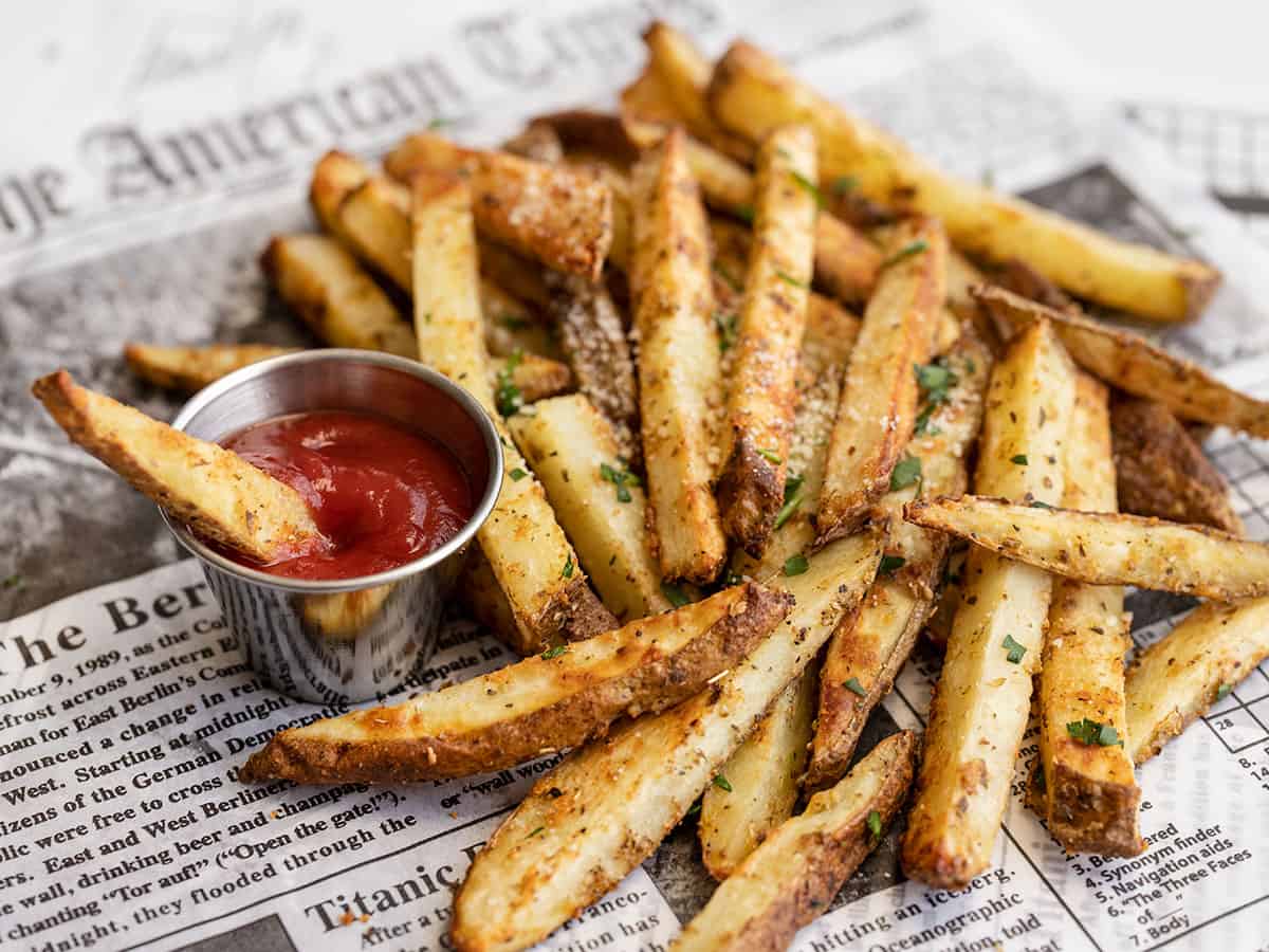 Side view of a pile of Garlic Parmesan fries with a small cup of ketchup
